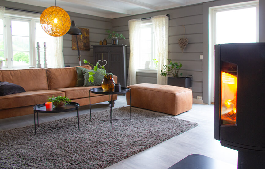 Brændeovn i grå stue med bindingsværksvægge og brun sofa