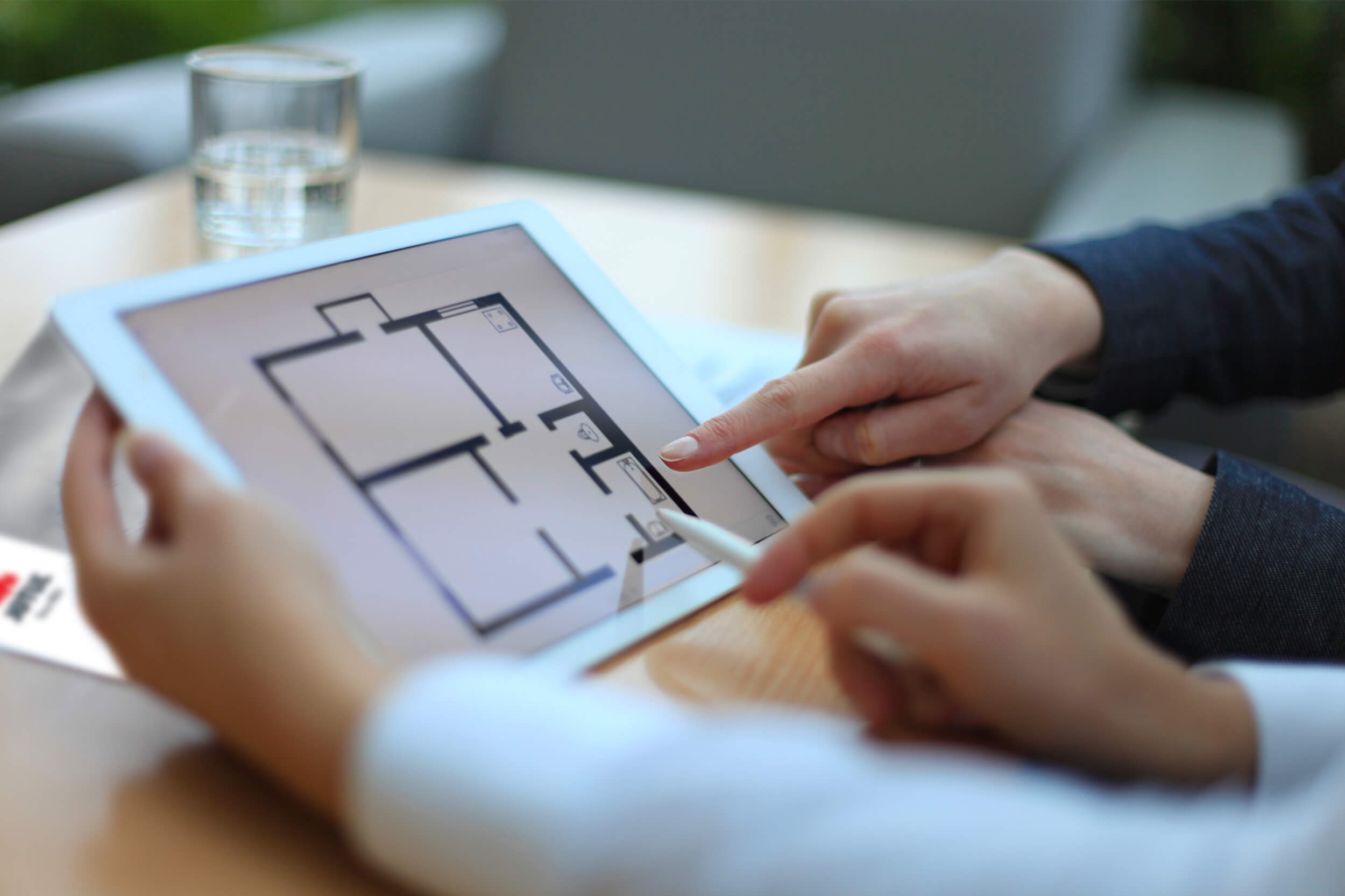Hænder, der peger på iPad med ark med rumfordeling i et hus.